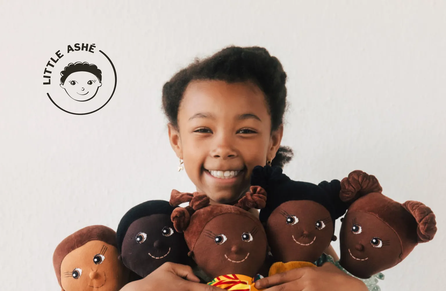 A happy girl holding several LITTLE ASHÉ dolls in her hands and a LITTLE ASHÉ in the top-left